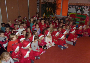 dzieci ubrane na czerwono, w czapeczkach mikołakowych podczas oglądania przedstaiwnia teatru WidziMiSię pt. "Piotruś Pan"