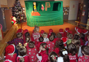 dzieci ubrane na czerwono, w czapeczkach mikołakowych podczas oglądania przedstaiwnia teatru WidziMiSię pt. "Piotruś Pan", dekoracja do przedstawienia