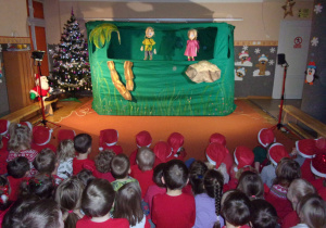 dzieci ubrane na czerwono, w czapeczkach mikołakowych podczas oglądania przedstaiwnia teatru WidziMiSię pt. "Piotruś Pan", dekoracja do przedstawienia