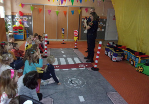 Strażnik Miejski opowiada dzieciom o sygnalizacji wskazując czerwone światło