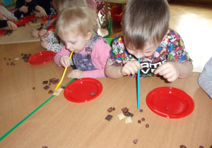 dzieci za pomocą słomek przekładają płatki śniadaniowe ze stolika na talerzyki
