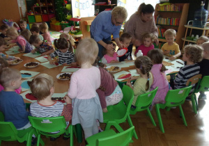 dzieci siedząc przy stoliczkach wykonują pracę plastyczną z papieru i płatków śniadaniowych