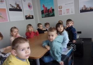 dzieci przy stołach słuchają opowiadania proacownika muzeum