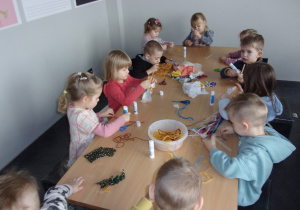 grupa dzieci przy stole wykonuje prace z wykorzystaniem włóczki i materiałów tekstylnych