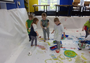 dzieci w białych koszulkach podczas malowania farbami rękoma i stopami na dużych arkuszach papieru