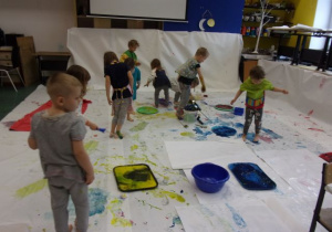 dzieci w białych koszulkach podczas malowania farbami rękoma i stopami na dużych arkuszach papieru