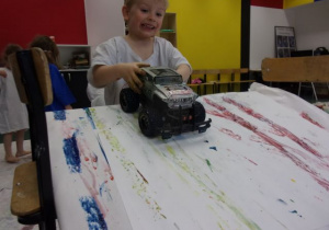 chłopiec maluje oponami samochodu na białych arkuszach papieru