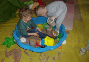 chłopcy w baseniku podczas zabawy materiałami sypkimi