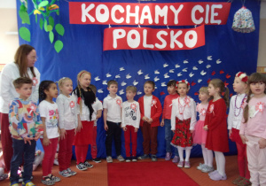 Juniorzy śpiewaja piosenką na tle dekoracji "Kocham Cię Polsko"