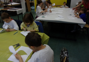 dzieci siedzą przy dużym stole nakrytym białym papierem i zółtą folią