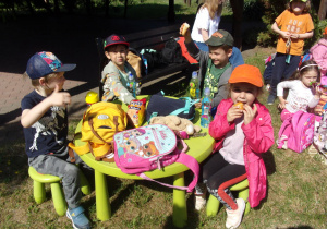 dzieci przy stoliczku jedzą ciasteczka i piją napoje