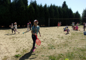 dziewczunka z rakietką, w tle dzieci bawiące się w piasku