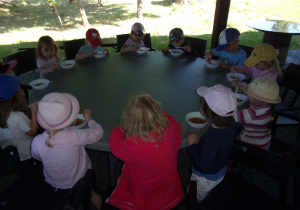 dzieci przy okrągłych stołach jedzą zupę z soczewicy z boczkiem i ziemniakami