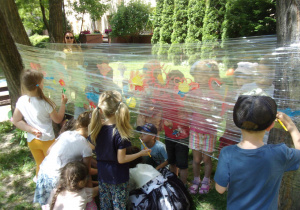 dzieci malują farbami plakatowymi na foliach rozwieszonych w ogrodzie przedszkolnym