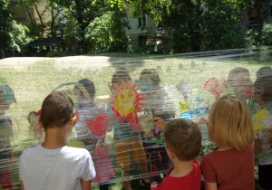 dzieci malują farbami plakatowymi na foliach rozwieszonych w ogrodzie przedszkolnym