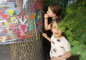 chłopiec z dziewczynką malują farbami na foli w ogrodzie przedszkolnym