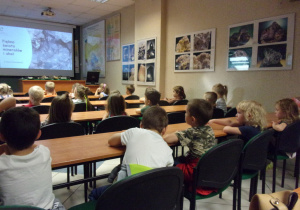 Żaczki sidzą w ławkach i oglądają prezentację dotyczącą eksponatów Muzeum Geologicznego