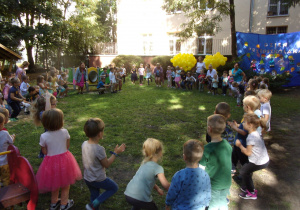 dzieci ze wszystkich grup w kole uczestniczą w zabawach z okazji Dnia Przedszkolaka w ogrodzie przedszkolnym