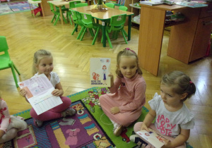trzy dziewczynki oglądają książeczki "Dziel się uśmiechem"