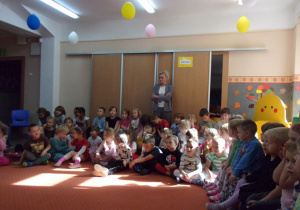 dzieci na sali gimnastycznej podczas słuchania czytanych przez pracowników przedszkola wierszy
