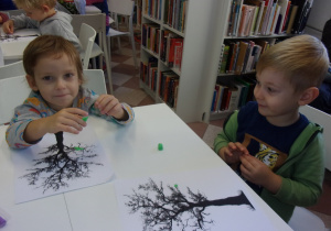 dwoje chłopców przy stoliku przykleja z plasteliny liście na sylwecie drzewa