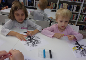 dwie dziewczynki przy stoliku przyklejają z plasteliny liście na sylwecie drzewa