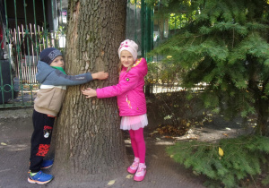 dwoje dzieci obejmuje drzewo w ogrodzie przedszkolnym