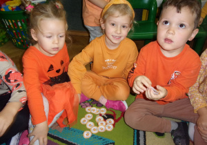 dzieci ubrane na pomaraczowo biorą udział w zabawie dydaktycznej, przeliczają koła z nadrokowanymi dyniami