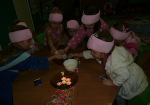 dziewczynki w szflafroczkach z opaskami na głowach przy stoliczku z zapalonymi świeczkami