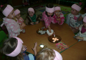 dziewczynki w szflafroczkach z opaskami na głowach przy stoliczku z zapalonymi świeczkami, na stoliczku miseczki z ogórkami