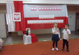 chłopiec z dziewczynką na tle dekoracji z okazji Święta Niepodległości recytują wiersz