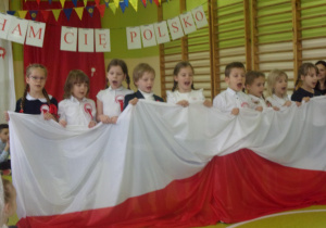 Juniorzy śpiewaja piosenkę trzymając w rękach flagę