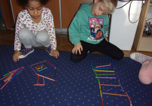 dwoje dzieci układa obrazek z wykorzystaniem kredek