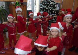 dzieci ubrane na czerwono w mikołajkowych czapeczkach tańczą na sali gimnastycznej