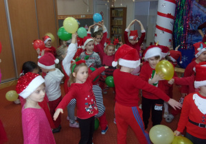 dzieci ubrane na czerwono w mikołajkowych czapeczkach podczas zabawy z balonami
