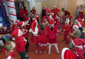 dzieci ubrane na czerwono w mikołajkowych czapeczkach tańczą na sali gimnastycznej