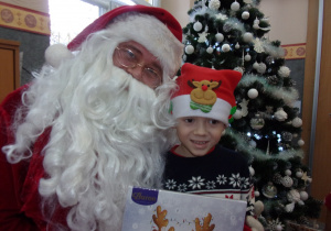 chłopiec stoi obok Mikołaja, trzyma w rękach prezent