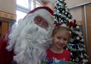 dziewczynka stoi obok Mikołaja, trzyma w rękach prezent