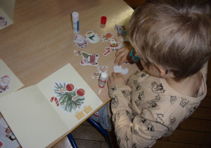chłopiec przy stoliczku przykleja na kartce świątecznej elementy