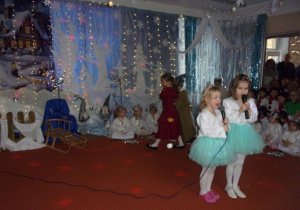 dwie dziewczynki w turkusowych spódniczkach i białych bluzkach śpiewają piosenkę