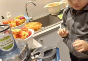 chłopiec wkłada pokrojone jabłka do sokowirówki
