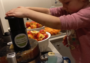 dziewczynka wkłada pokrojone jabłka do sokowirówki
