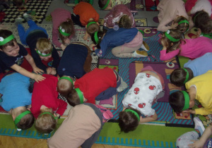 zabawa ruchowa na dywanie - dzieci z opaskami żabek na głowach