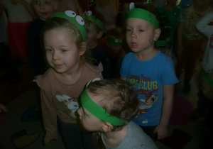 dzieci w opaskach żabek na głowie słuchają opowieści nauczycielki
